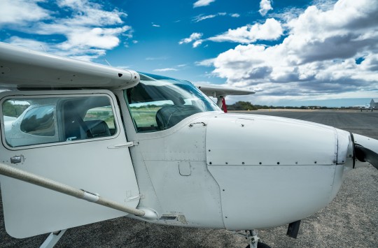 A small aeroplane sits on an aerodrome apron with its door open