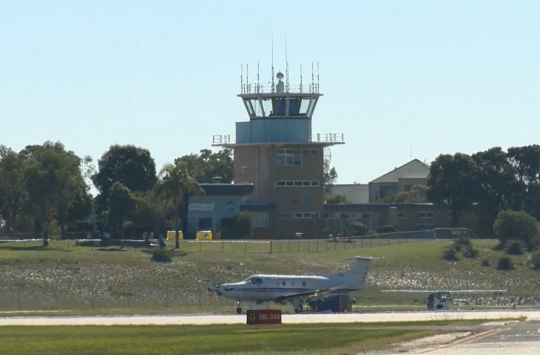 An aeroplane on a runway with an air traffic control tower in the background