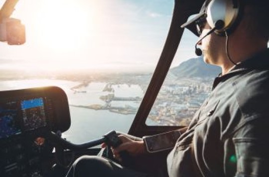 A pilot flying other the water of a harbour, with the sun shining brightly in the sky in front of him