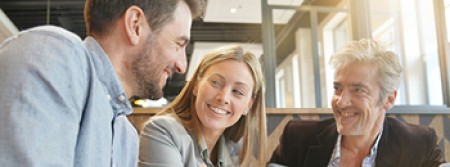 A smiling man and woman looking at a smiling man they're sitting next to