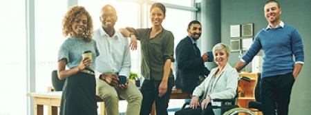 A group of men and women of different ethnicities in an office. One woman is in a wheelchair.