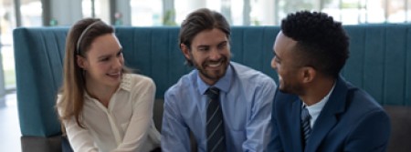 A white man and woman sitting next to a black man and smiling at him while he gives a presentation on his laptop