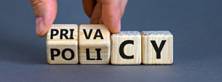 A pair of fingers holding a pair of wooden blocks at an angle with two more blocks sitting next to them. The faces visible spell out "privacy" and "policy"