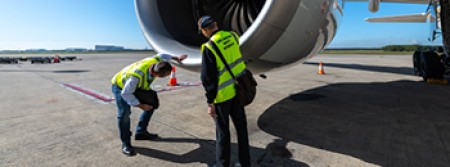 A pair of CASA inspectors wearing high-visibility jackets examine an airliner's engine