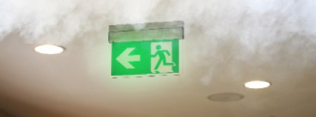 An exit sign glowing through smoke gathering at the ceiling
