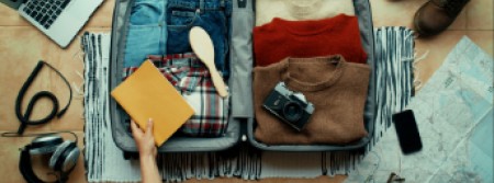 A person's hand holding a book as they pack a suitcase