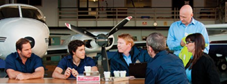 A several people holding a work meeting in a hangar