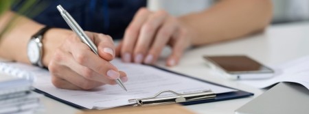 The hands of someone writing on forms held on a clipboard