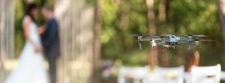 A drone hovering in the air while a couple gets married behind it