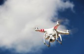 Drone flying against white clouds in a blue sky.