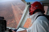 A pilot flying a plane coming in for a landing at a dirt runway