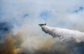 An aeroplane surrounded by smoke dropping water onto a bushfire below