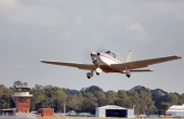 A small aeroplane taking off, with airport buildings visible behind it