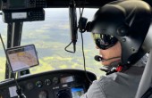 A pilot wearing a helmet flying over the countryside