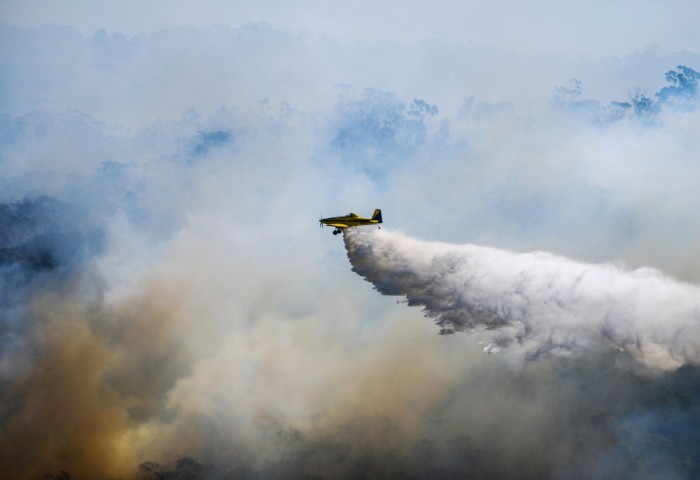 An aeroplane surrounded by smoke dropping water onto a bushfire below