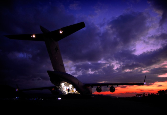 An aeroplane with its rear cargo door open and interior lights on as the sun sets behind it