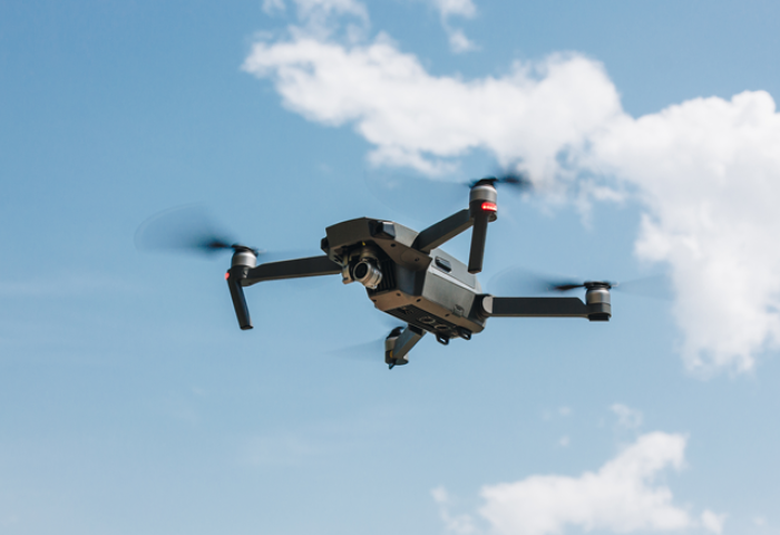 A drone flying through the blue sky, with a cloud behind it