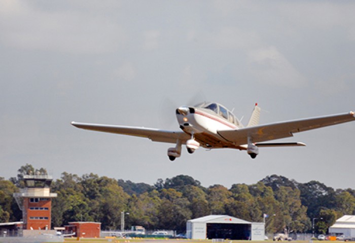A small aeroplane taking off, with airport buildings visible behind it