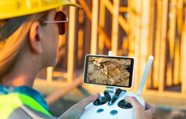 Female Unmanned Aircraft System (UAV) quadcopter drone pilot with controller inspecting new house framing