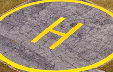 A helicopter landing zone - flat concrete square with a yellow circle and a large "H" painted on it