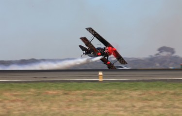 Avalon airshow biplane flying over runway with contrail