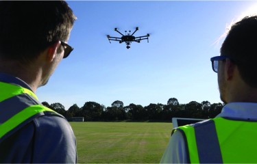 Two men in high-visibility jackets looking at a drone they are flying
