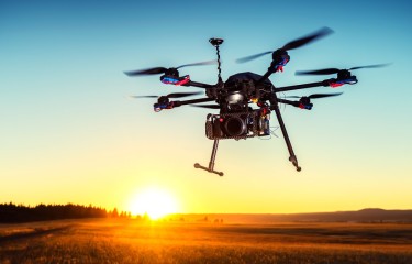 A multirotor drone silhouetted against the darkening sky of a sunset