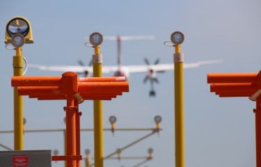 Poles with aerodrome equipment on them with a plane landing in the background