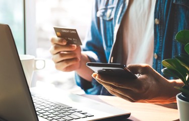 A woman sitting a laptop computer with a cell phone and a credit card in her hands