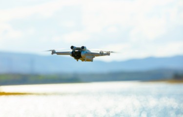 A white RPA flying with a lake in the background