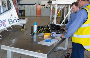 Two maintenance engineers in a hangar examining paperwork and a computer