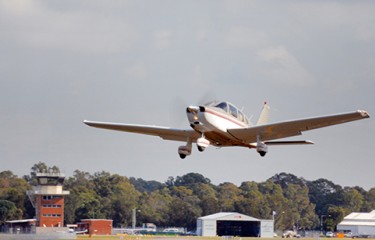 A small aeroplane taking off, with airport buildings visible behind it