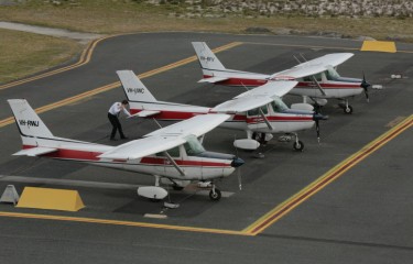 Three identical small aeroplanes lined up next to each other on the aircraft apron, as a pilot inspects the middle one