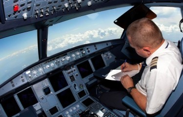 A pilot fills out documentation in the cockpit of a flying aircraft